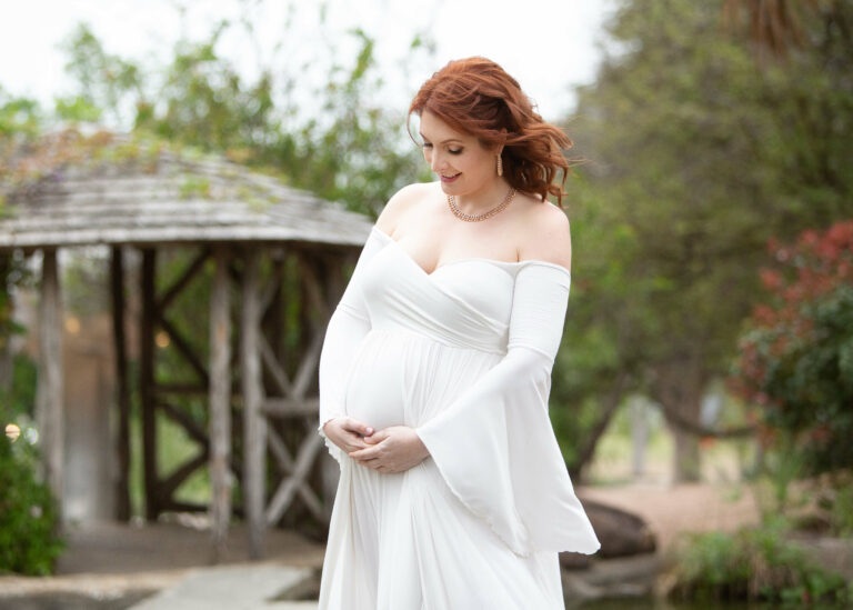 A pregnant woman in a white dress poses at the McNay in Alamo Heights during photo session