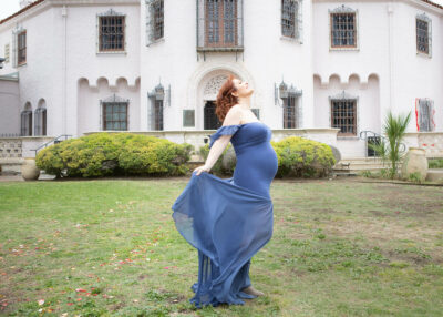 A pregnant woman in a blue dress posing in front of a castle.