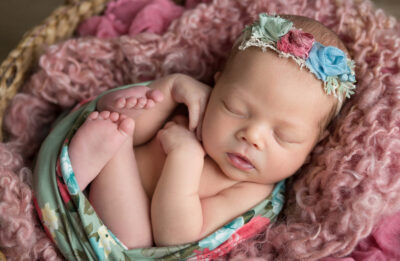 A baby girl sleeping in a basket with a floral headband.