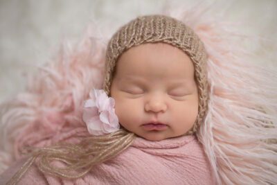 A baby girl in a pink hat sleeping on a fluffy blanket.