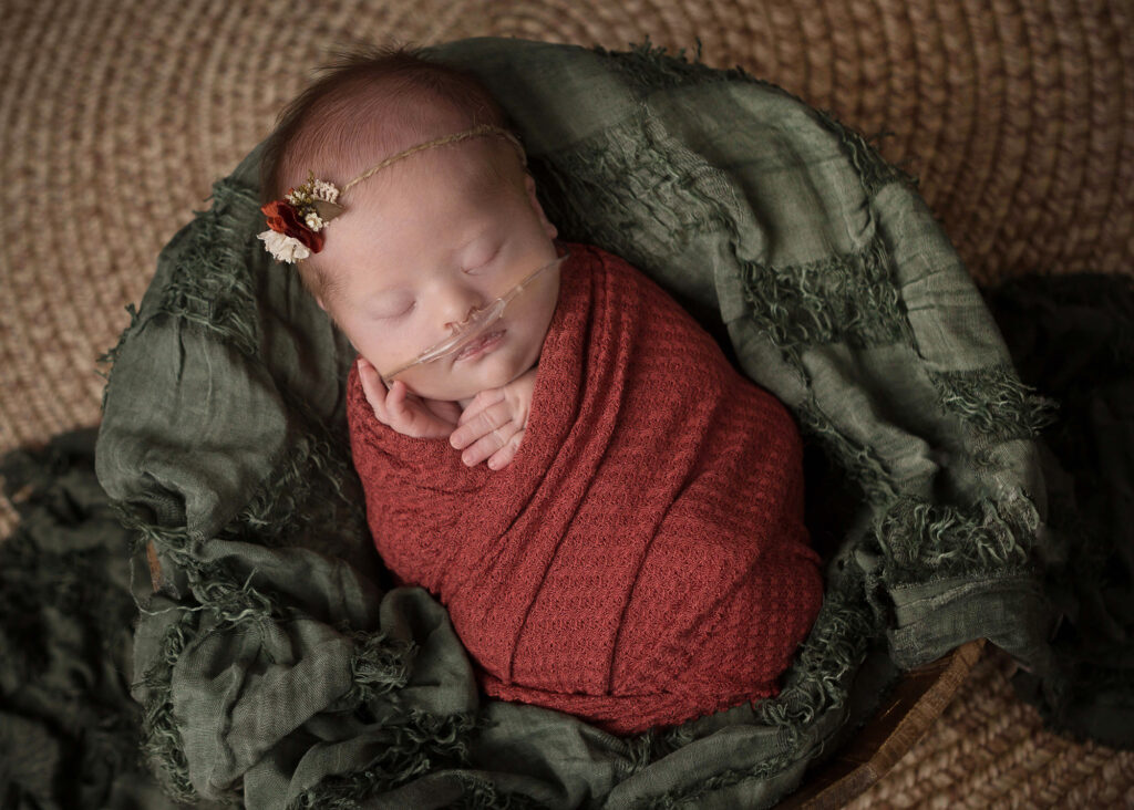 A baby girl wrapped in a red blanket in a basket.