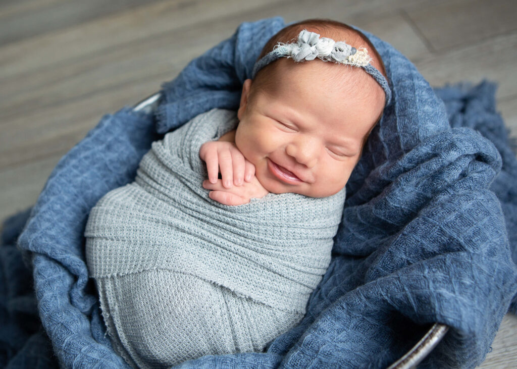 A newborn girl is wrapped in a blue blanket and smiling.