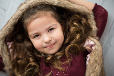 A little girl in a fur coat posing for a photo.