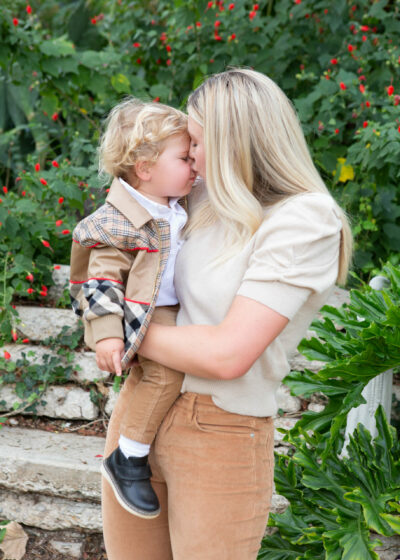A woman kissing her son in front of a garden.
