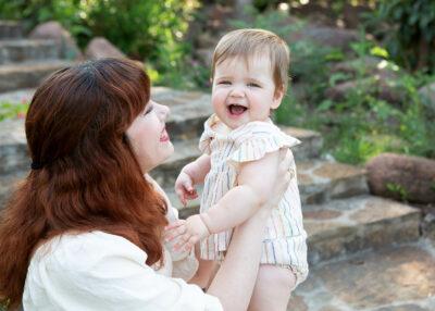 A woman laughing while holding a baby on a set of steps.