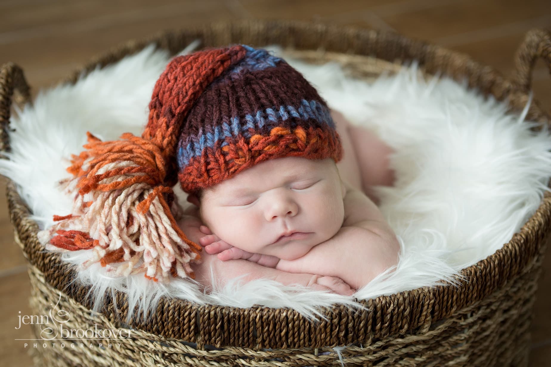 close up of newborn boy in knitted cap snuggling on fur during photo session