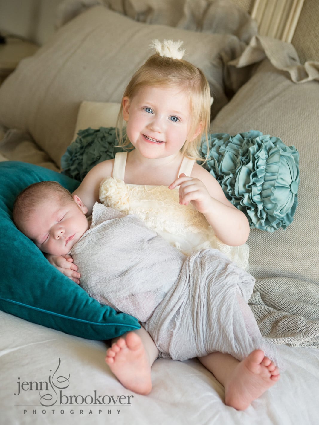 excited big sister smiling and holding her new baby brother at home during newborn session