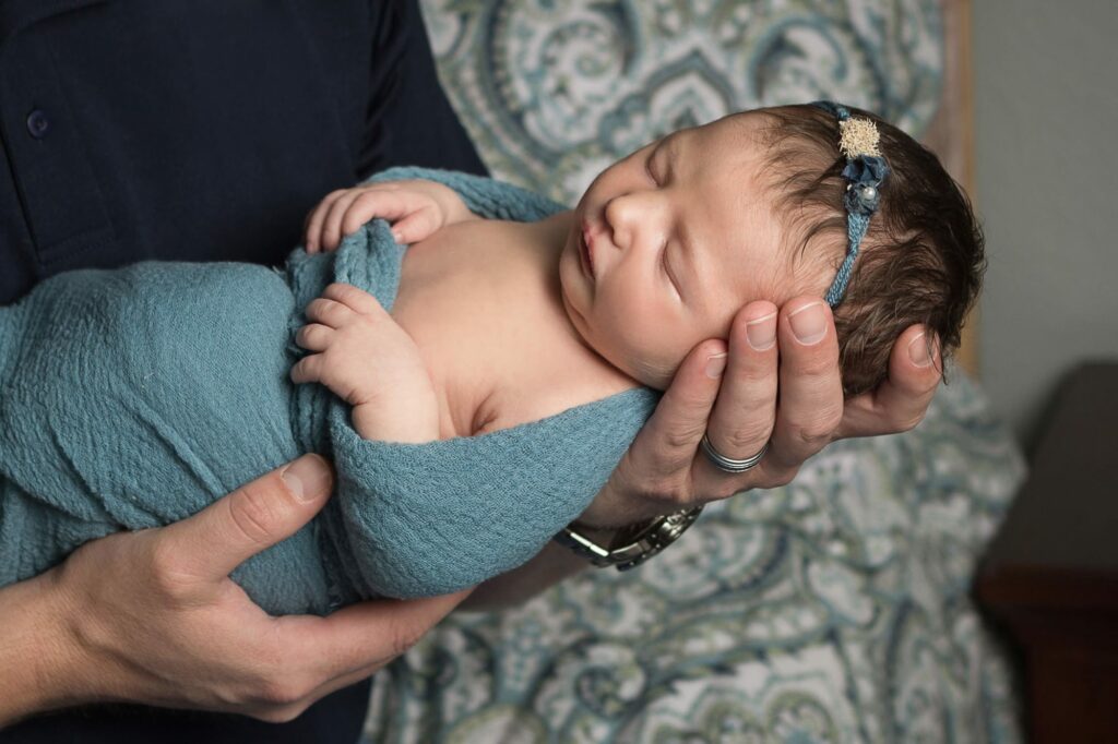 dad in navy shirt holding baby girl in teal wearing a Devoted Knits headband