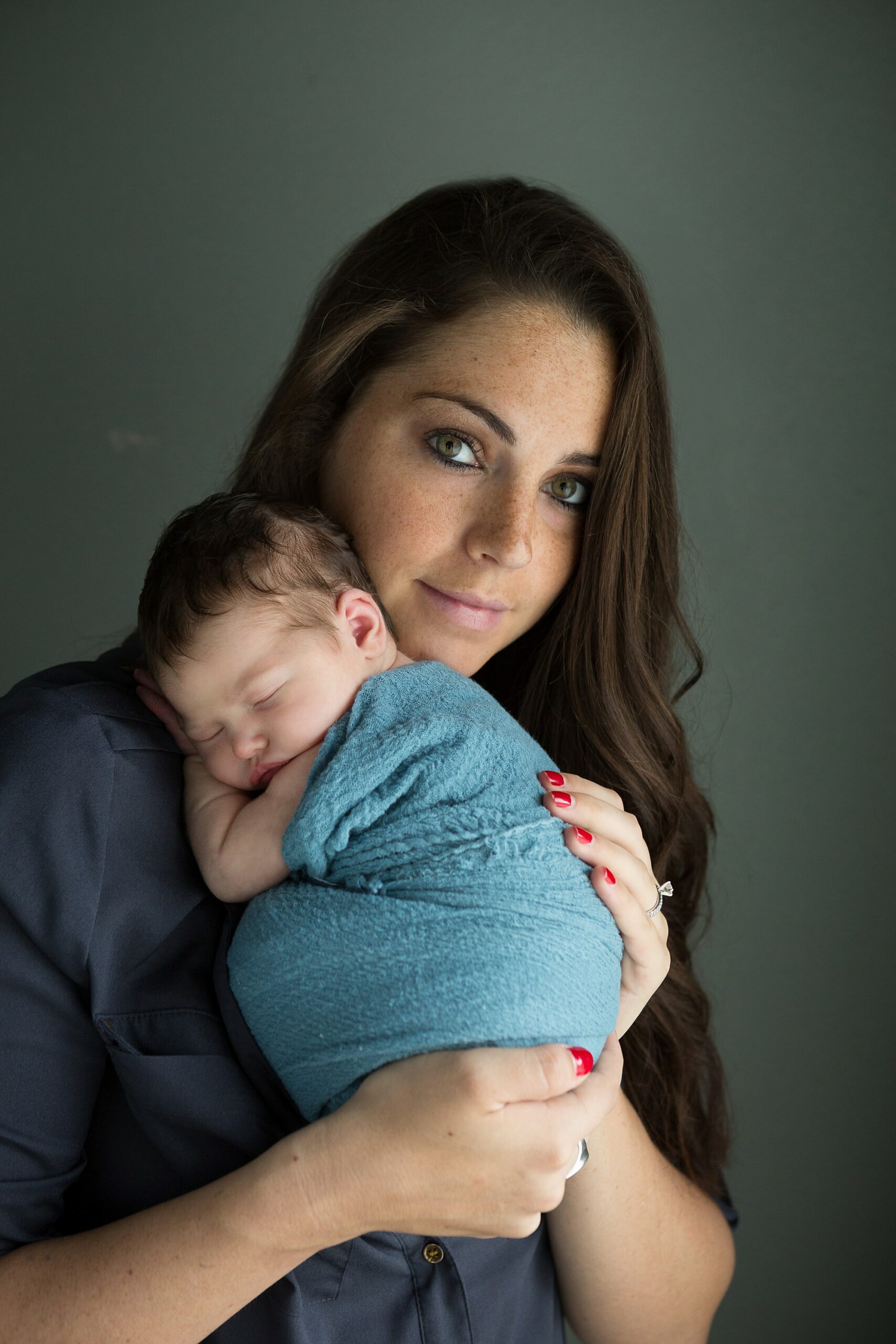 mom looking at camera holding baby wrapped in teal during newborn portrait session
