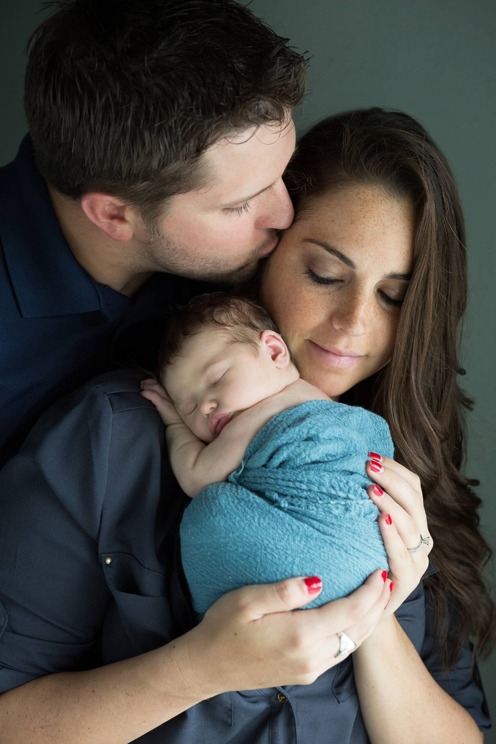 dad kissing mom holding newborn baby girl at home during photo session
