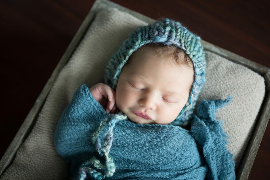 newborn in teal hat and wrap during photo session at home