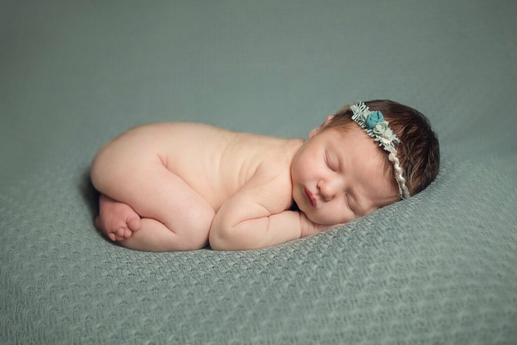 newborn curled up asleep on sage blanket