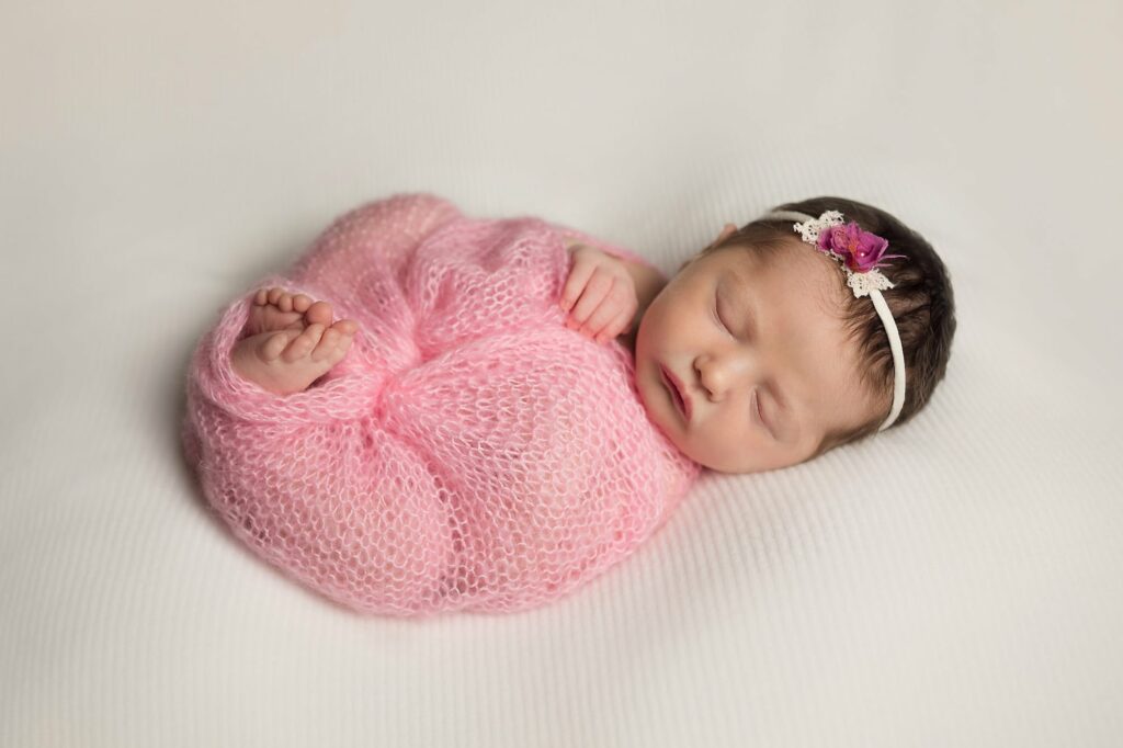 newborn wrapped up in pink on white backdrop