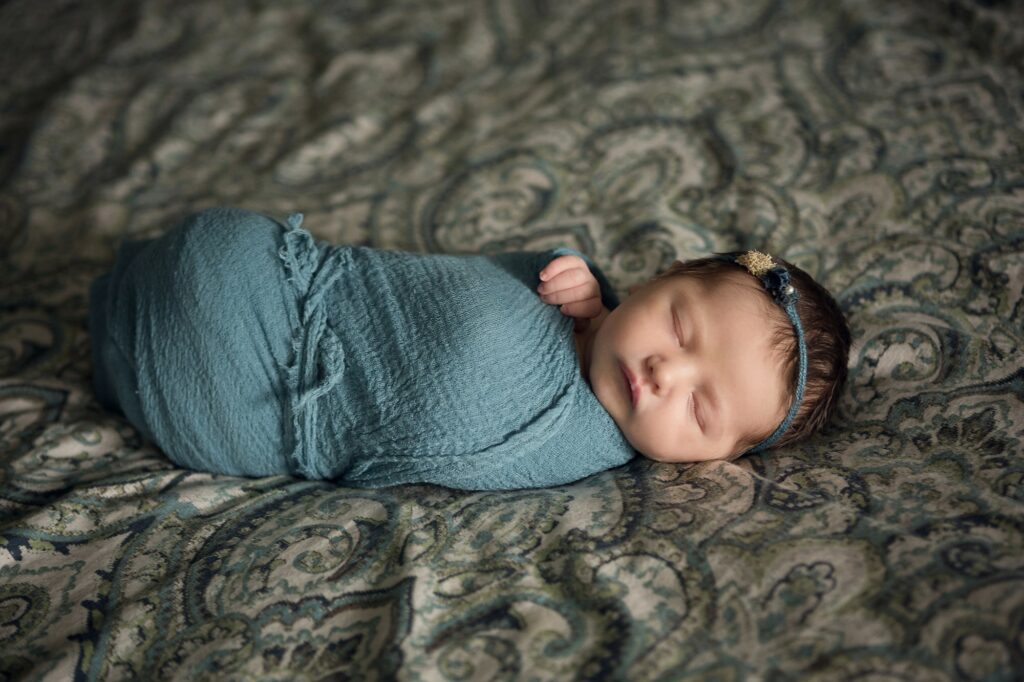newborn baby on bed at home wrapped in teal and wearing a Devoted Knits Headband