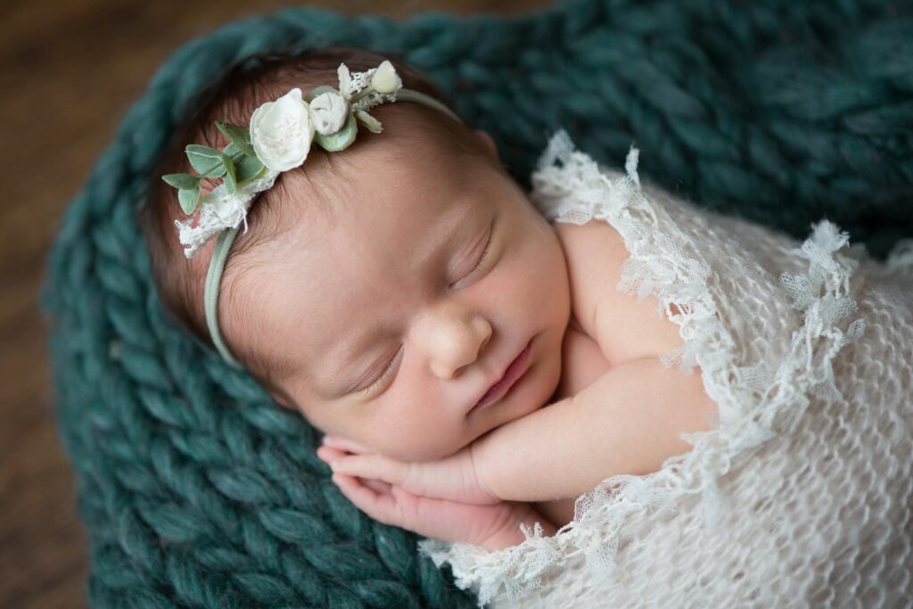A newborn girl sleeping in a green blanket.