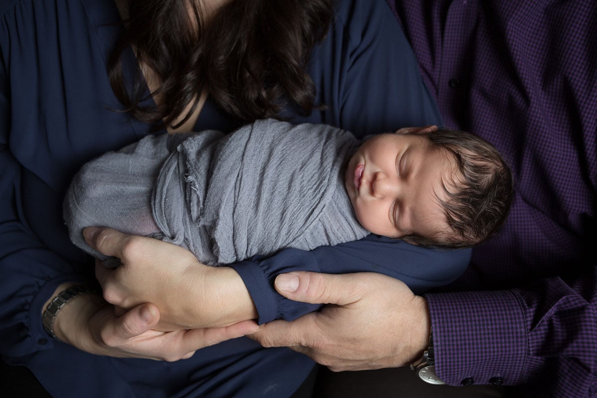 newborn boy held by mom and dad during family session, wrapped in gray close up