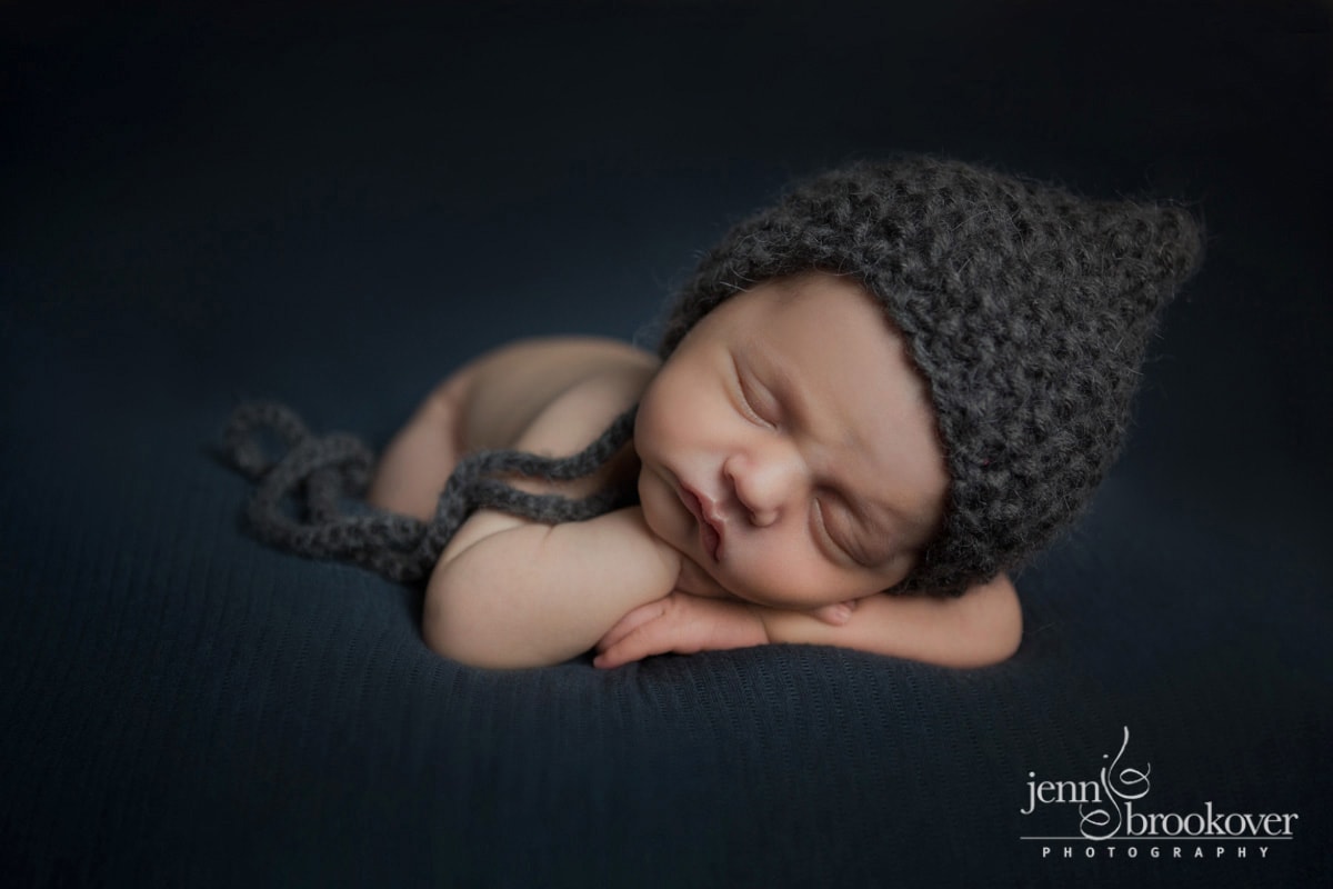 newborn boy on a navy background in a dark gray knitted hat taken during his session with Jenn Brookover at home in Alamo Heights Texas