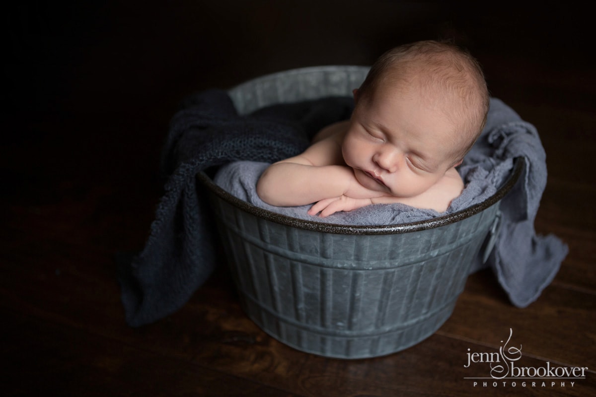 sweet baby boy newborn asleep in a bucket surrounded by gray during his newborn session at home in Alamo Heights