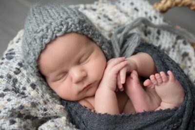 A newborn baby sleeping in a grey knitted hat.