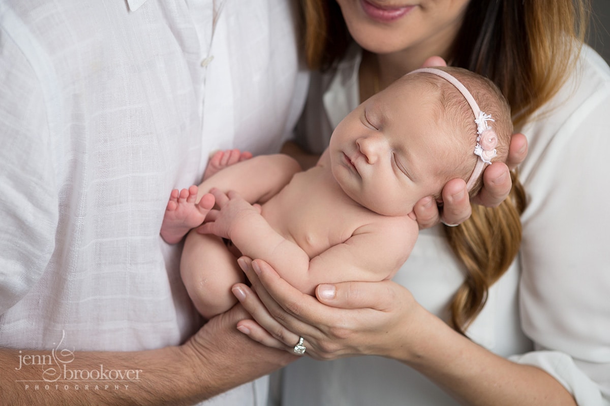 close up of newborn baby girl in parent's hands taken during portrait session with Jenn Brookover