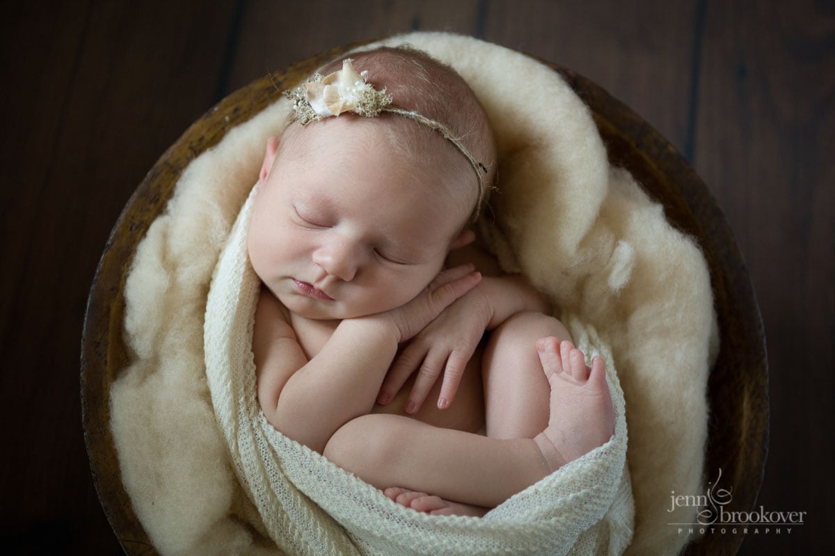 cuddled up newborn in cream wrap set in a bowl taken by Jenn Brookover in San Antonio