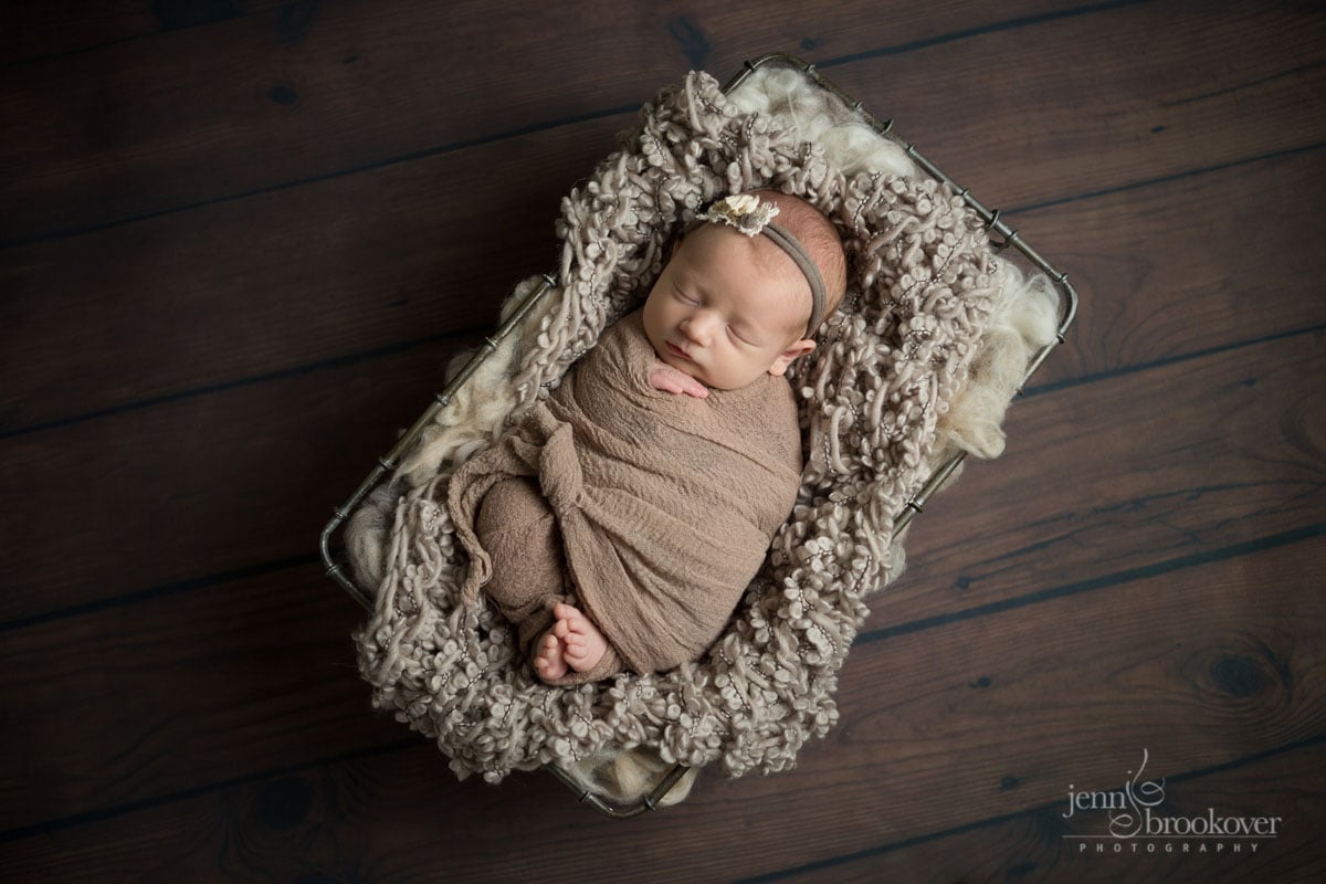 baby girl swaddled in taupe resting in a basket asleep during her newborn photo session with Jenn Brookover