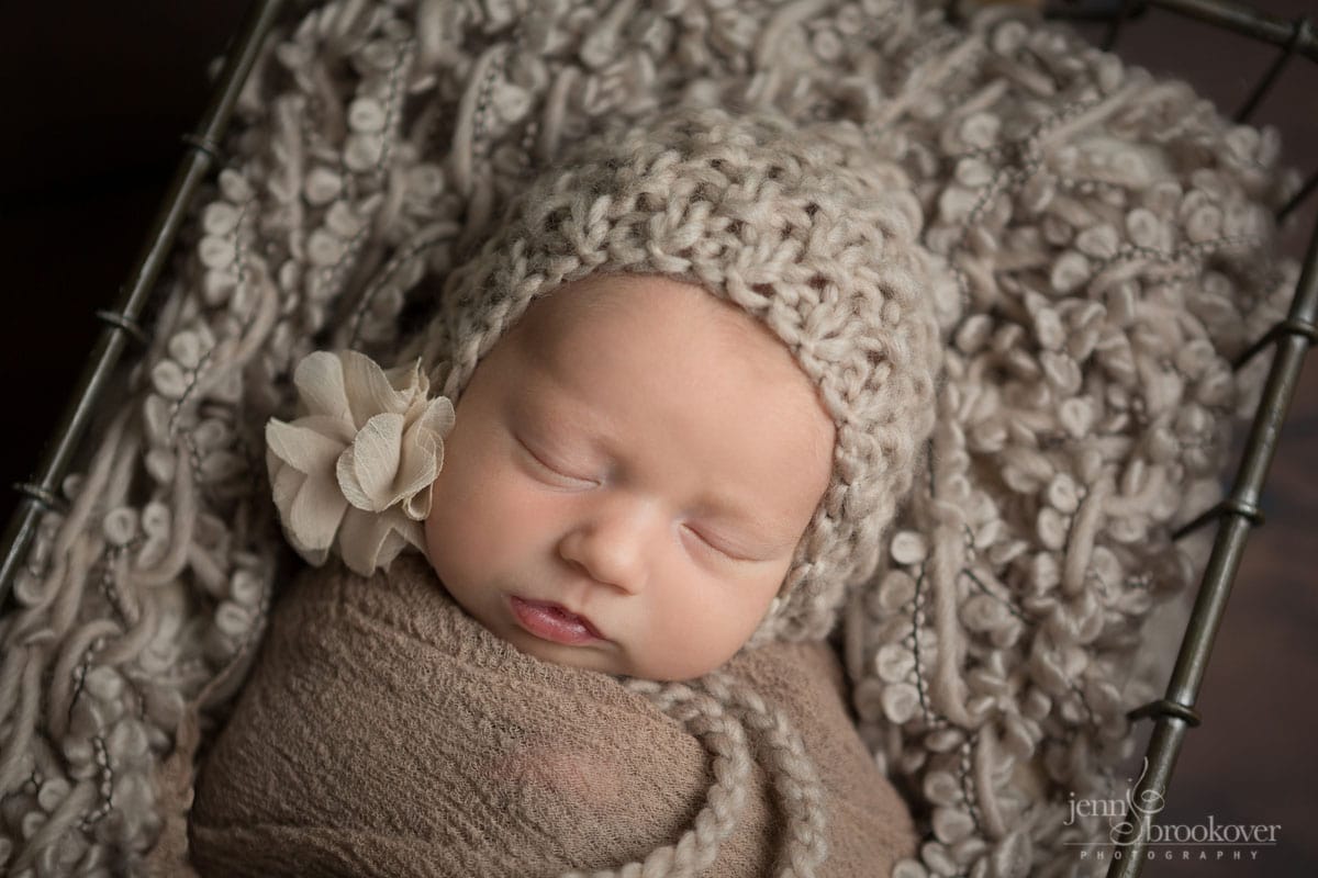 close up of newborn face wearing taupe knitted bonnet with flower asleep during her photo shoot with Jenn Brookover in San Antonio