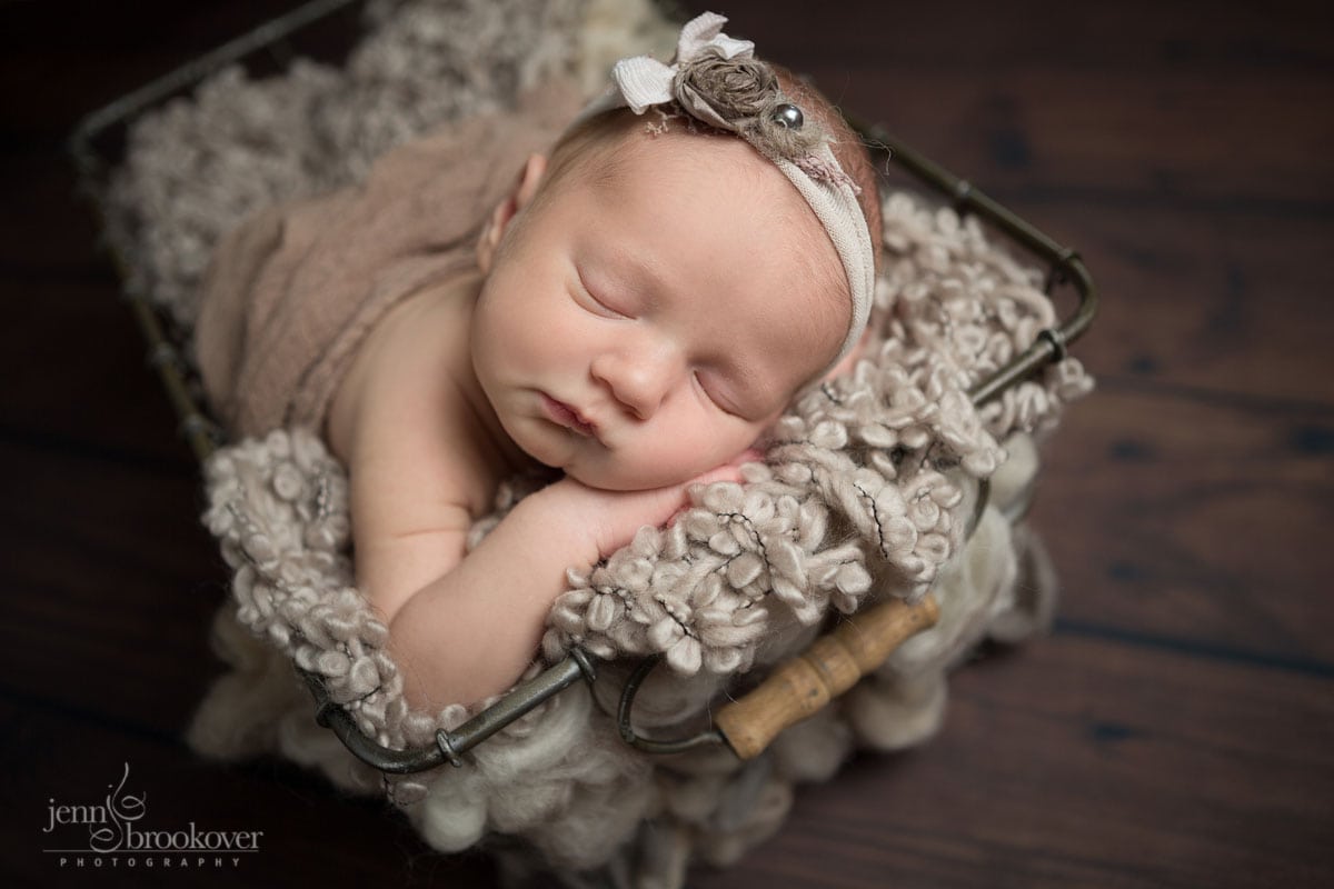 sleeping newborn in a metal basket wrapped in taupe for her newborn photo session with Jenn Brookover