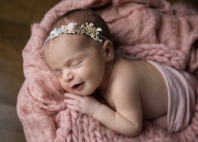 A newborn girl is smiling in a pink blanket.