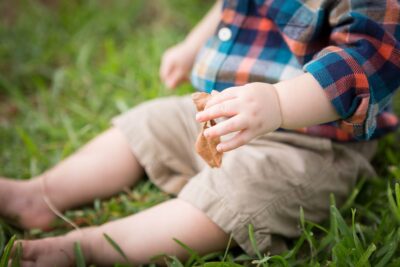 A baby boy is sitting in the grass with a toy in his hands.