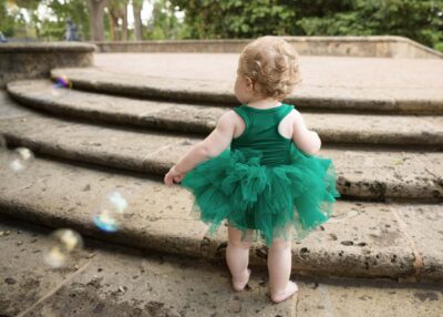 A baby girl in a green tutu standing on steps.