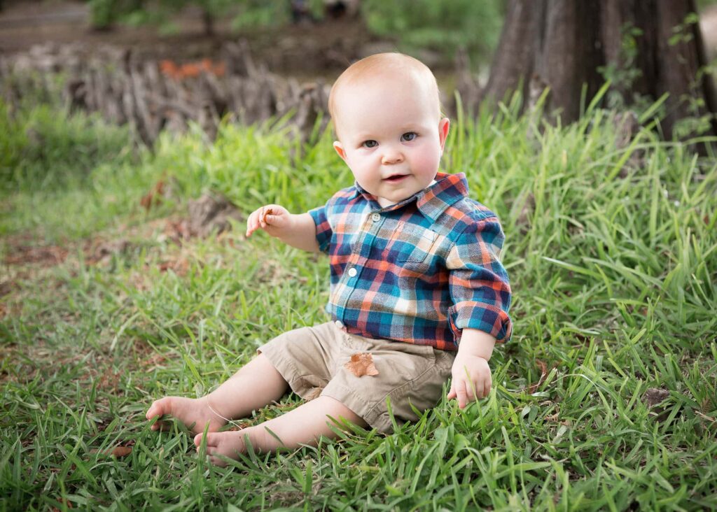 A baby sitting on the grass in front of a tree.