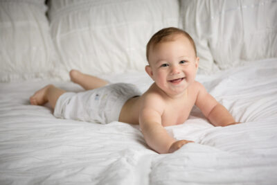 A baby laying on a white bed with a smile on his face.