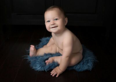 A baby sitting on a blue furry rug.