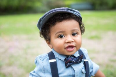 A baby boy wearing suspenders and a hat.