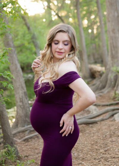 A pregnant woman in a purple dress posing in the woods.