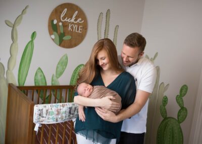 A man and woman are holding a baby in a cactus themed nursery.