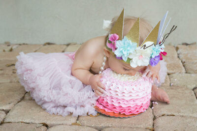 A baby girl in a pink tutu eating a cake.