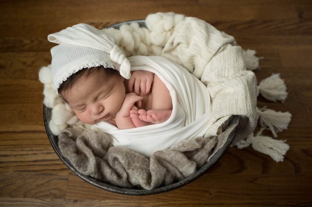 A newborn sleeping in a basket on a wooden floor.