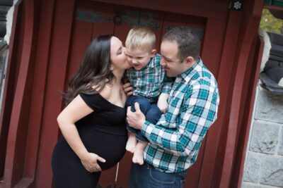 A pregnant woman kisses her son in front of a red door.