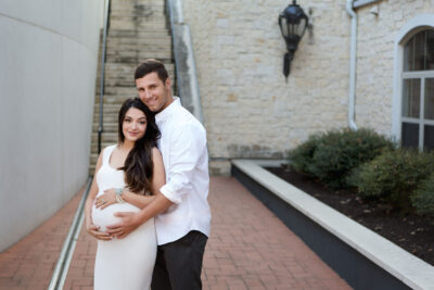 A pregnant couple posing in front of a building.