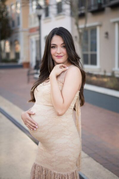 A pregnant woman in a beige dress posing for a photo.