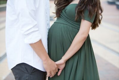 A couple in a green maternity dress holding hands.