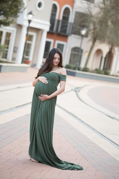 A pregnant woman in a green dress poses in front of a building.