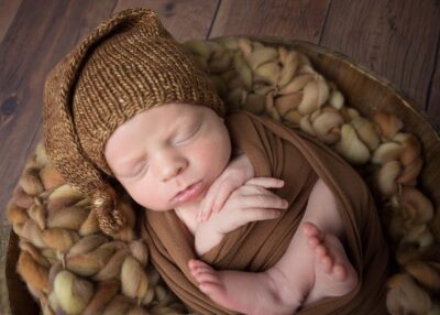 A baby boy in a brown hat is sleeping in a bowl.