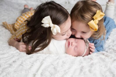 A group of girls kissing a newborn baby.