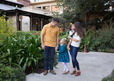 A family is standing in a courtyard with their daughter.
