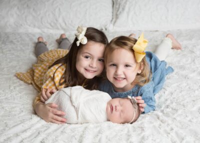 A group of girls lying on a white blanket with a newborn baby.