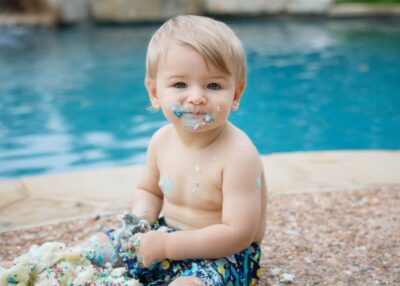 A baby boy eating cake in front of a pool.