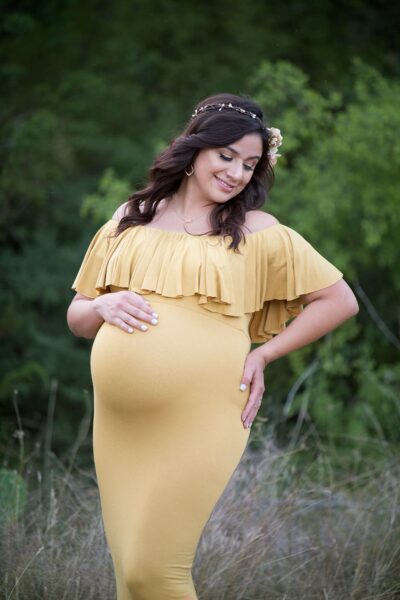 A pregnant woman in a yellow dress posing in a field.